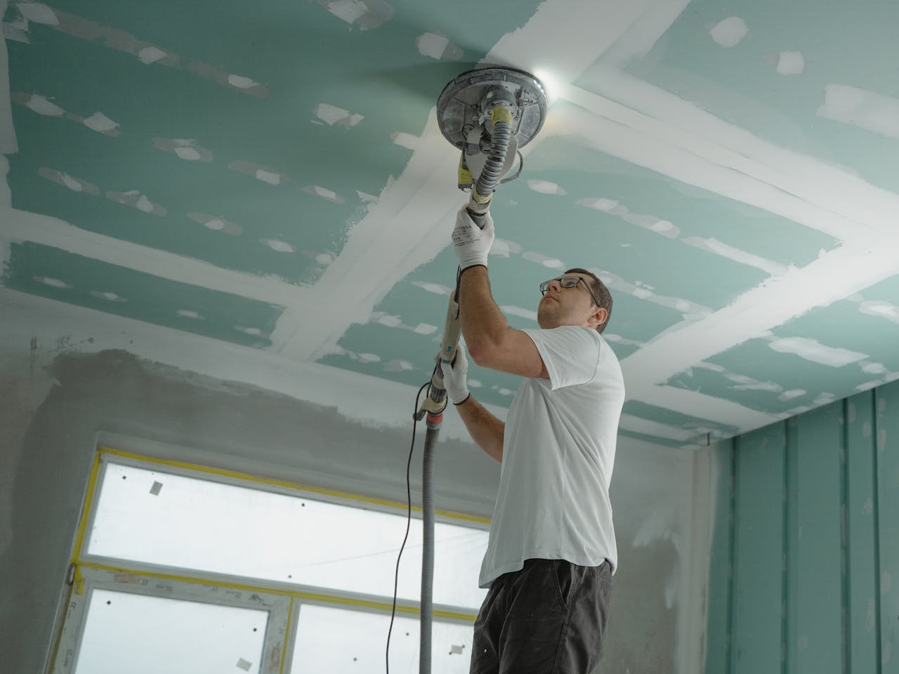 why-choose-us A professional worker sanding the ceiling during a home renovation project. Indoor construction setting.